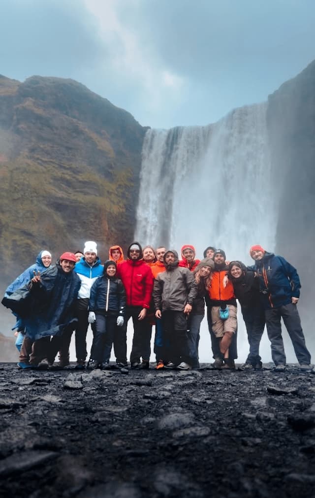 Un viaggio di gruppo WeRoad posa per una foto su un terreno roccioso davanti a una grande cascata nebbiosa.