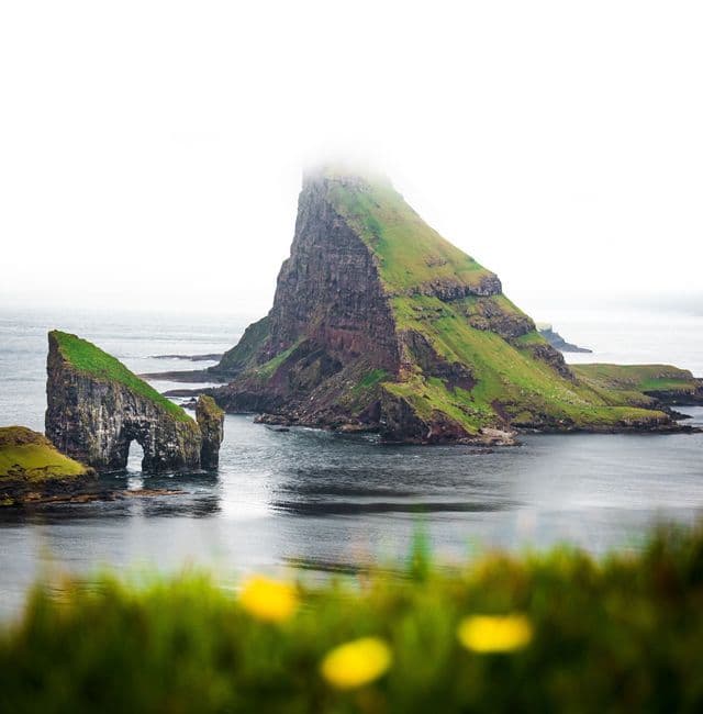Due grandi faraglioni ricoperti di verde si ergono dall'oceano, uno con un arco naturale e l'altro con la cima avvolta nella nebbia.