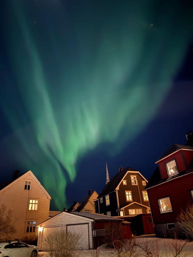 L'aurora boreale verde illumina il cielo notturno sopra una città innevata con case tradizionali.