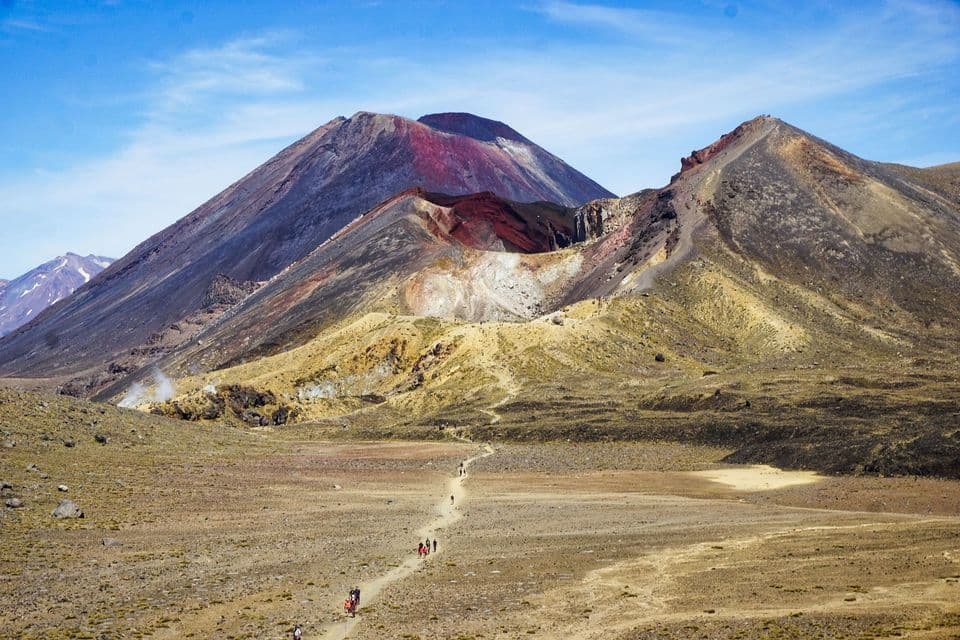 Un gruppo WeRoad fa trekking su un sentiero in una valle arida, verso montagne vulcaniche colorate sotto un cielo azzurro.
