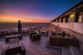 A person standing on a wooden deck of a building, looking out at the ocean during a colorful sunset.