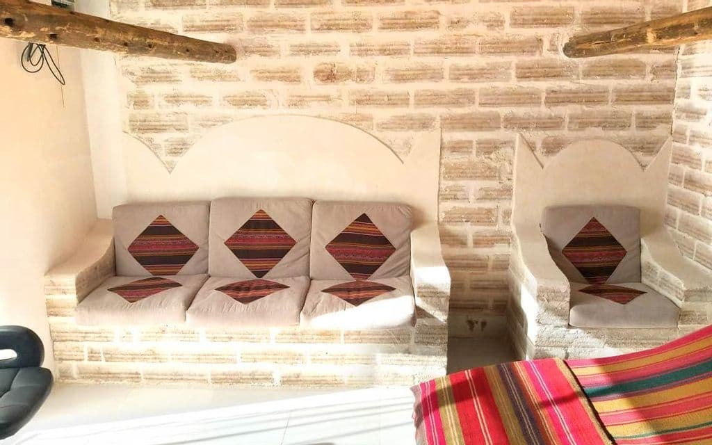 Un intérieur de chambre rustique avec un canapé et un fauteuil intégrés dans un mur de briques de couleur claire, agrémentés de coussins à motifs.