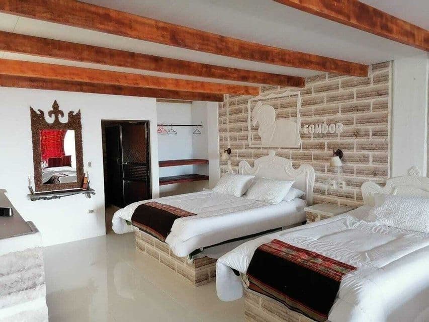 L'intérieur d'une chambre d'hôtel avec deux lits, un mur d'accent en briques de sel et un plafond avec des poutres en bois apparentes.