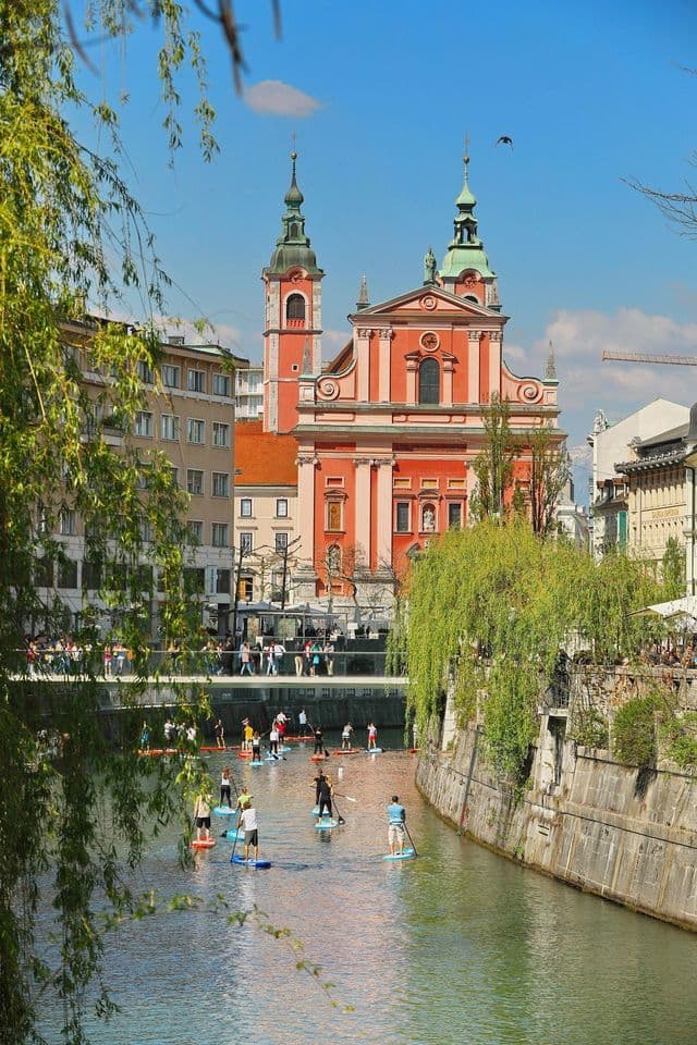 Un viaje en grupo de WeRoad haciendo paddleboard en un río urbano, con una gran iglesia rosa y un puente de fondo.