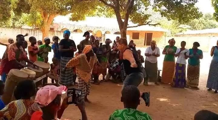 Un partecipante a un viaggio di gruppo WeRoad balla in cerchio con la gente del posto mentre altri suonano i tamburi e battono le mani in un villaggio.
