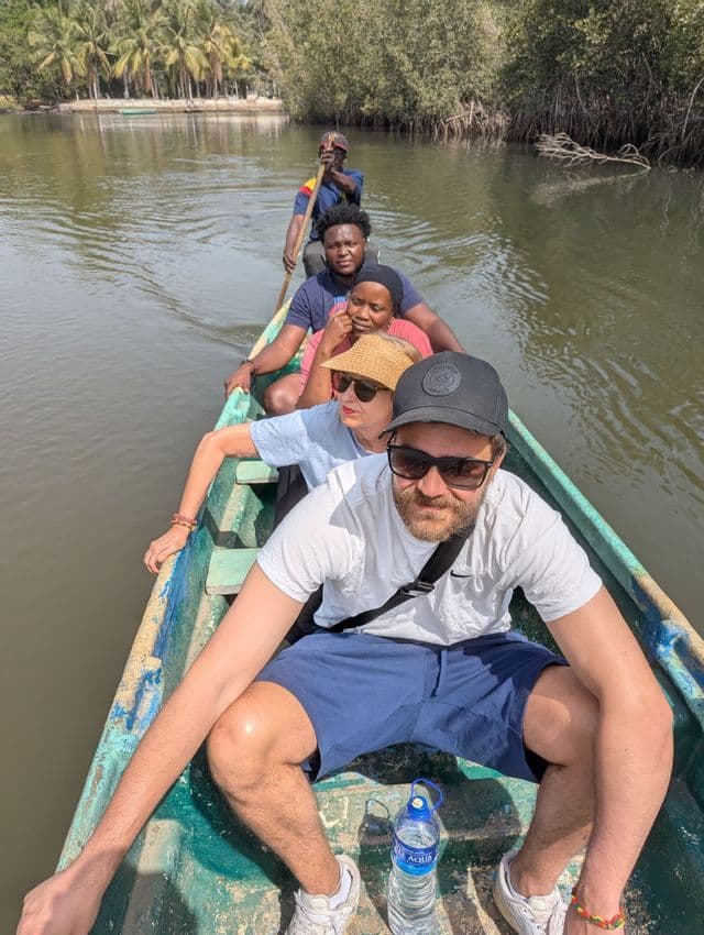 Un gruppo WeRoad naviga in una lunga canoa di legno lungo un fiume fiancheggiato da lussureggianti mangrovie.