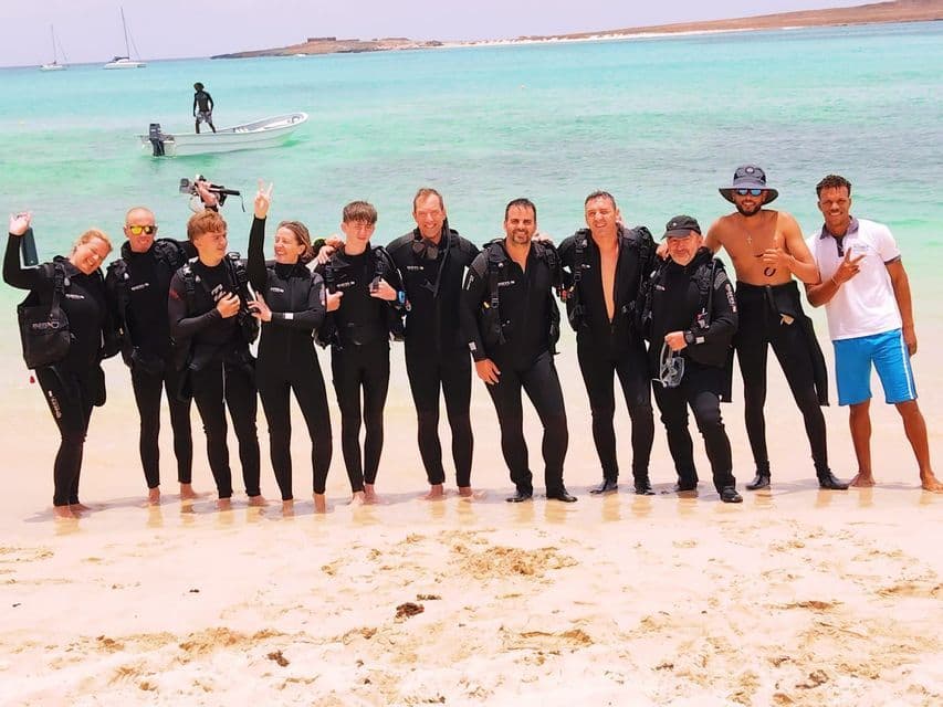 Un viaggio di gruppo WeRoad di subacquei in mute in posa per una foto su una spiaggia sabbiosa vicino ad acqua turchese.