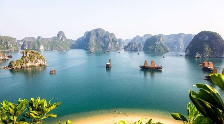 Una vista panoramica di diverse imbarcazioni tradizionali che solcano una baia tranquilla, costellata di grandi faraglioni carsici ricoperti di verde.