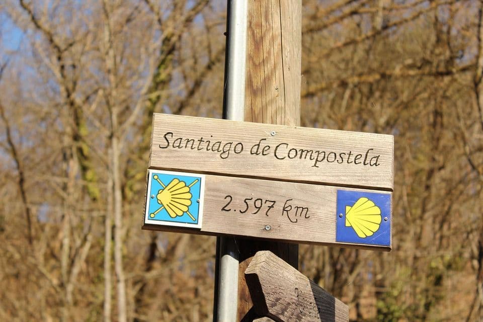 Cartello in legno per Santiago de Compostela, 2.597 km, con simboli a conchiglia.
