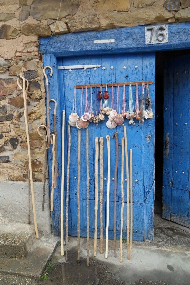 Bastoni da passeggio in legno e collane di conchiglie di capesante sono esposti in vendita contro una porta blu brillante incastonata in un muro di pietra.