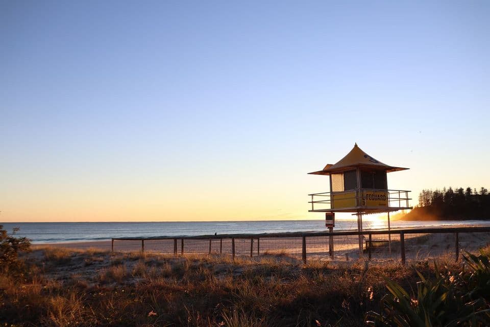 Una torre di salvataggio gialla si erge su una spiaggia sabbiosa all'alba, affacciata sull'oceano calmo sotto un cielo sereno.