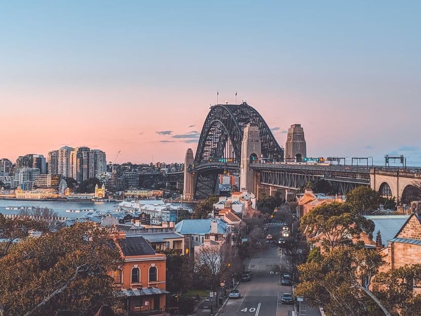 Sydney Harbour Bridge at sunset The Sydney Harbour Bridge and the city rooftops under a pink and orange sunset sky.