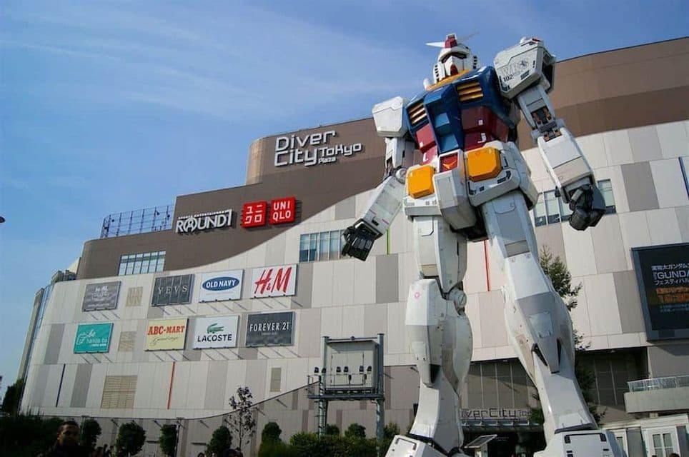 Una statua gigante del robot Gundam si erge di fronte all'edificio DiverCity Tokyo Plaza sotto un cielo azzurro e limpido.