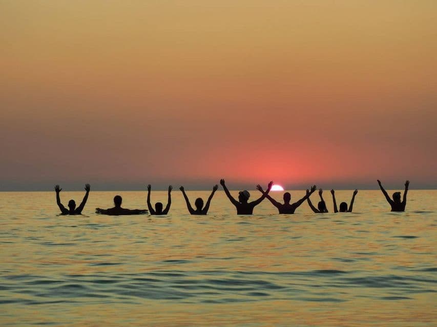 WeRoad Gruppenreise: Menschen als Silhouetten im Meer mit erhobenen Armen beim Sonnenuntergang.