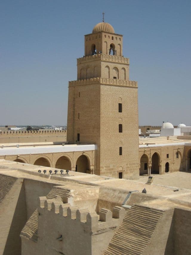 El alminar cuadrado de una mezquita, construido con piedra de color marrón claro, se eleva sobre los tejados circundantes y los patios abovedados.