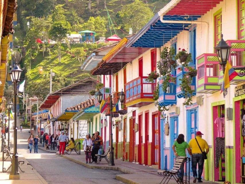 A vibrant street scene with people walking past brightly colored colonial buildings with wooden balconies.