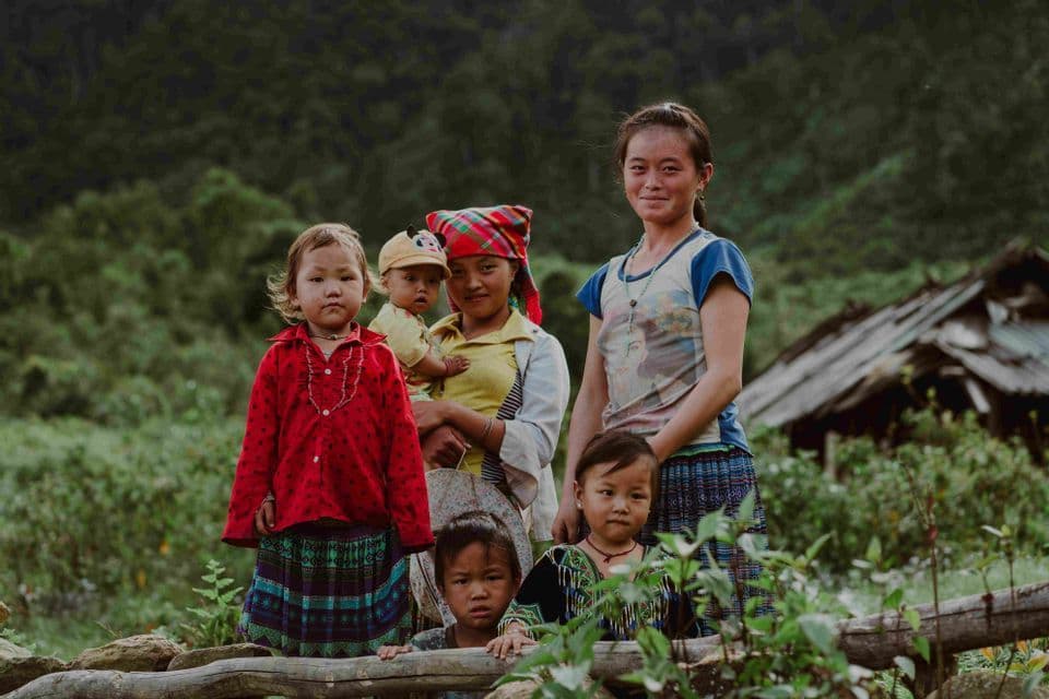 Una donna e cinque bambini con abiti colorati posano per una foto in un paesaggio rurale lussureggiante e verde.