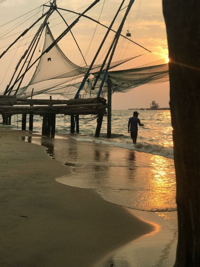 Una persona cammina sulla battigia accanto a una grande rete da pesca su una spiaggia al tramonto.