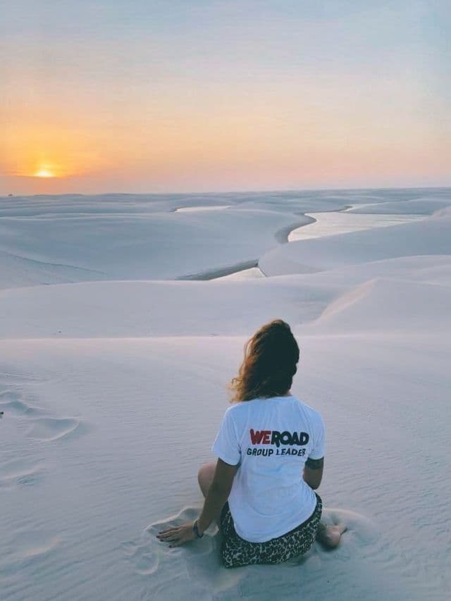Un chef de groupe WeRoad est assis sur une dune de sable blanc, regardant le coucher de soleil sur un paysage de lagons sinueux.
