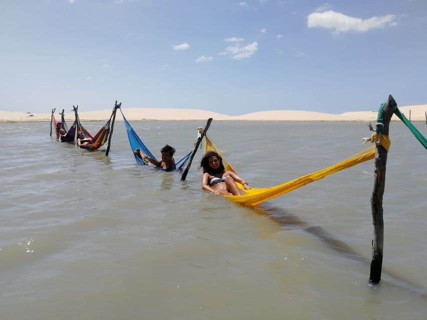 A WeRoad group trip relaxes in colorful hammocks suspended over a lagoon, with sand dunes in the background.