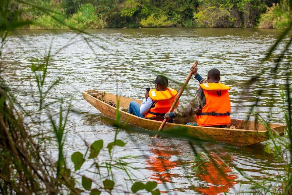 Due persone di un viaggio di gruppo WeRoad pagaiano una canoa di legno su un fiume tranquillo, indossando giubbotti di salvataggio arancioni.