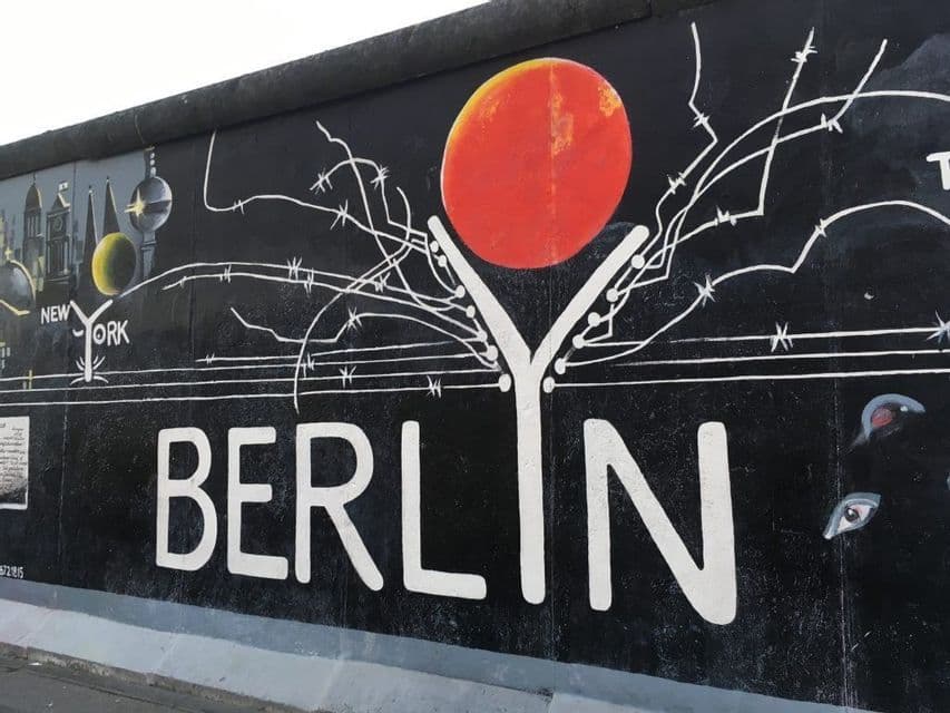 Un murale dipinto su un muro di cemento con la parola BERLINO in grandi lettere bianche sotto un sole rosso e grafiche di filo spinato.