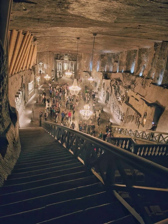 Vista aérea de una multitud reunida en una capilla subterránea excavada en la roca e iluminada por grandes candelabros de cristal.
