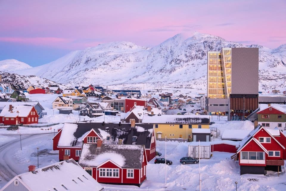 Case colorate in una città innevata ai piedi di grandi montagne sotto un cielo rosa.