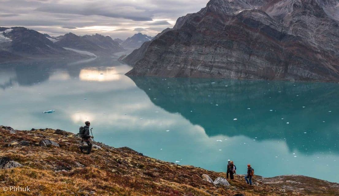 Un gruppo WeRoad di escursionisti su un pendio erboso che domina un lago glaciale turchese e le montagne sotto un cielo nuvoloso.