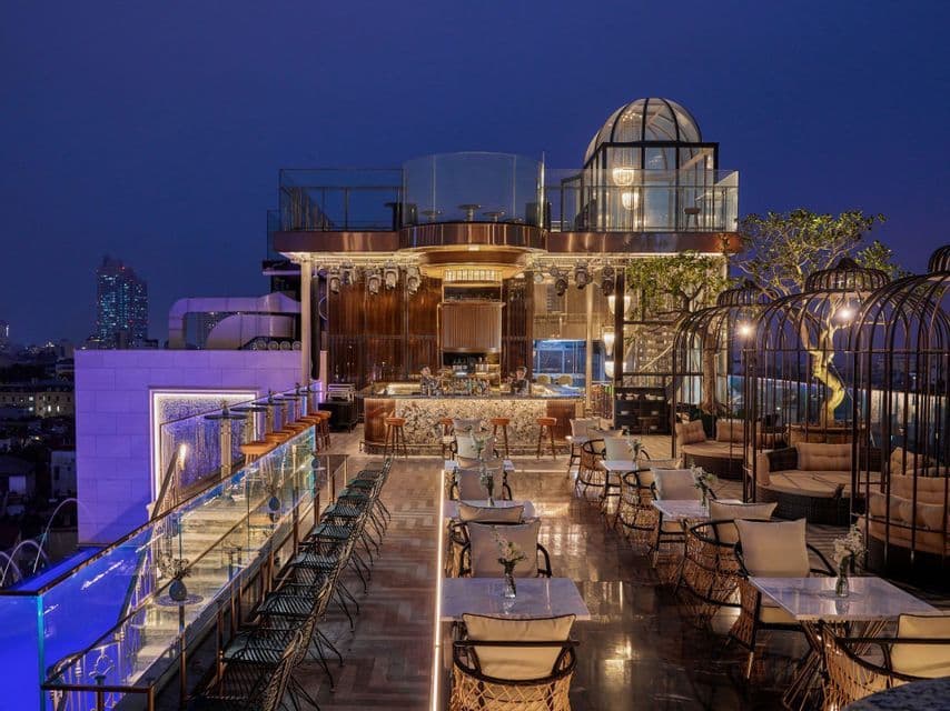 Un bar chic sur le toit, vide et illuminé au crépuscule, avec un long comptoir en marbre, des sièges modernes et une vue sur la ligne d'horizon de la ville.