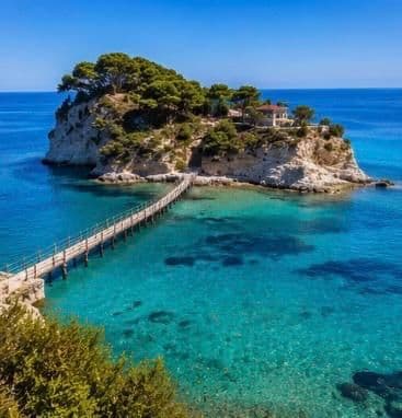 Una passerella di legno si estende su acque limpide e turchesi fino a una piccola isola alberata con una casa.