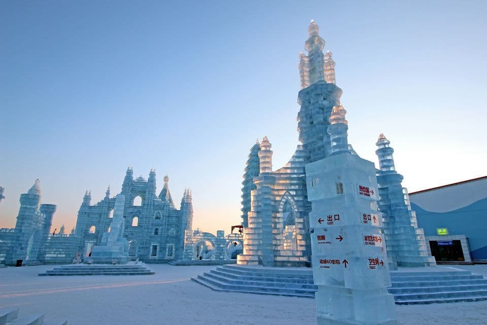 Grandi e intricati castelli di ghiaccio si ergono su una distesa innevata sotto un cielo sereno, con un cartello di ghiaccio in primo piano.