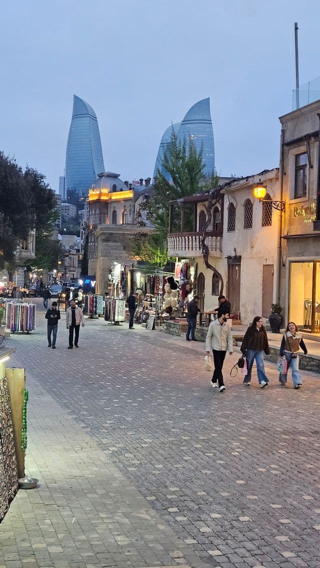 Eine WeRoad-Gruppe spaziert in der Abenddämmerung eine Kopfsteinpflasterstraße entlang, vorbei an Marktständen, mit modernen Wolkenkratzern im Hintergrund.