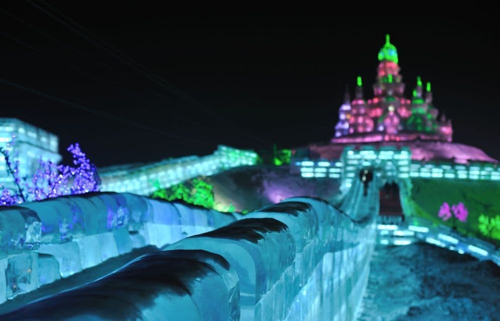 Una vista ravvicinata di una grande parete di ghiaccio illuminata con luci blu di notte, con un colorato castello di ghiaccio sullo sfondo.