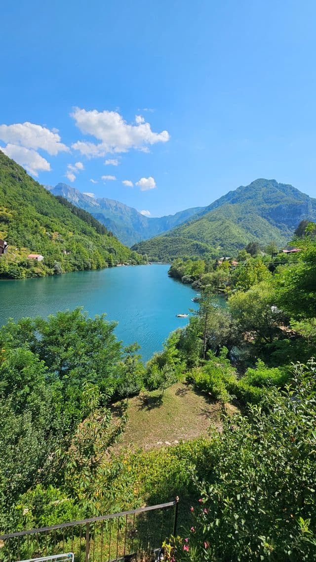 Eine Vogelperspektive auf einen gewundenen blauen See, umgeben von üppig grünen Bergen, unter einem klaren blauen Himmel mit einigen Wolken.