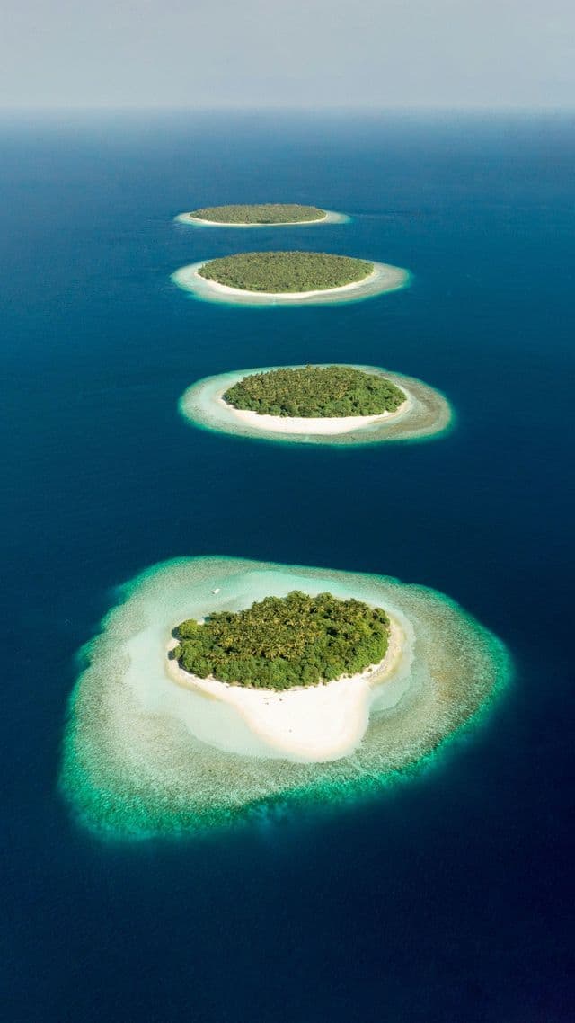 An aerial view of a line of small tropical islands with sandy beaches, surrounded by turquoise and deep blue water.