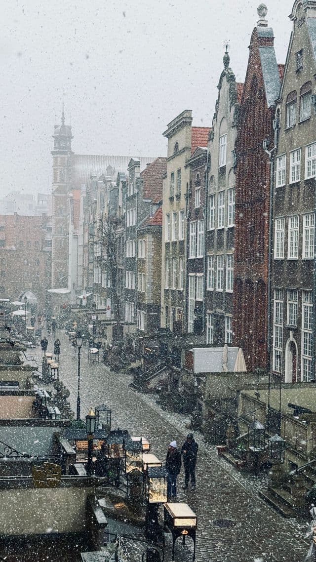 Vue plongeante d'une rue pavée dans une ville historique avec des gens marchant sous une forte chute de neige.