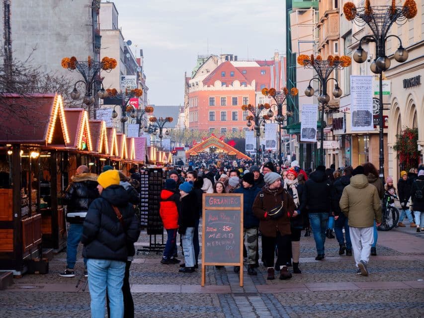 Une foule nombreuse parcourt une rue pavée, bordée d'étals de marché illuminés, lors d'un festival en plein air.