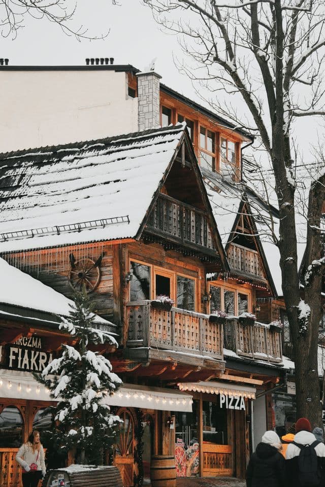 Un bâtiment traditionnel en bois avec des toits pentus et enneigés et des balcons ouvragés dans une rue d'hiver.