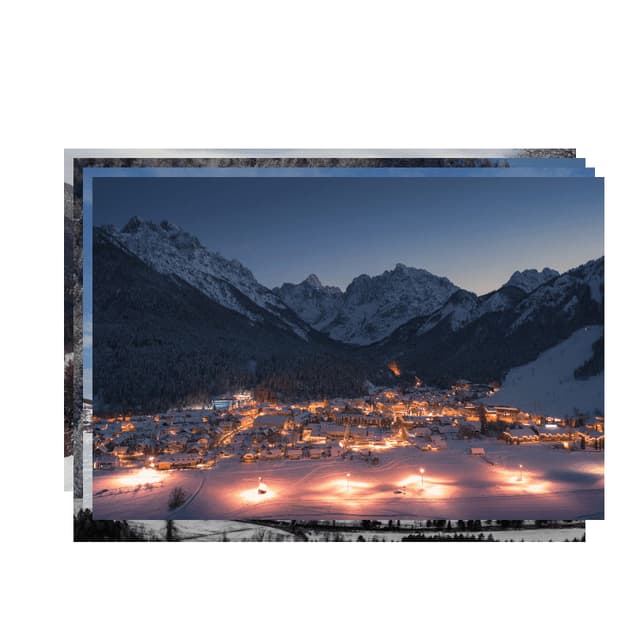Un villaggio illuminato in una valle innevata, immerso tra le montagne al crepuscolo.