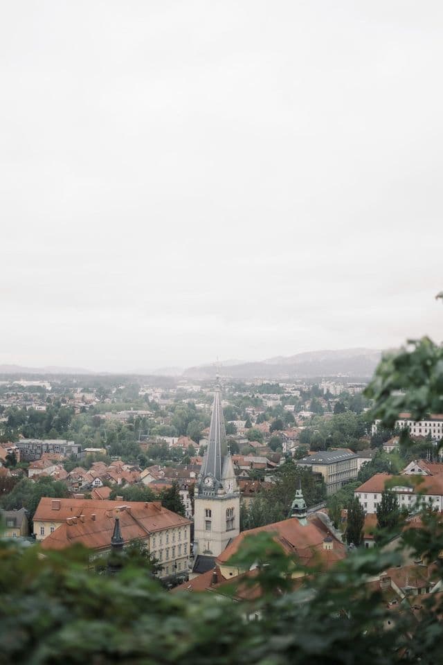 Una vista panoramica di una città con tetti rossi e un campanile di chiesa prominente che svetta sugli edifici in una giornata nuvolosa.
