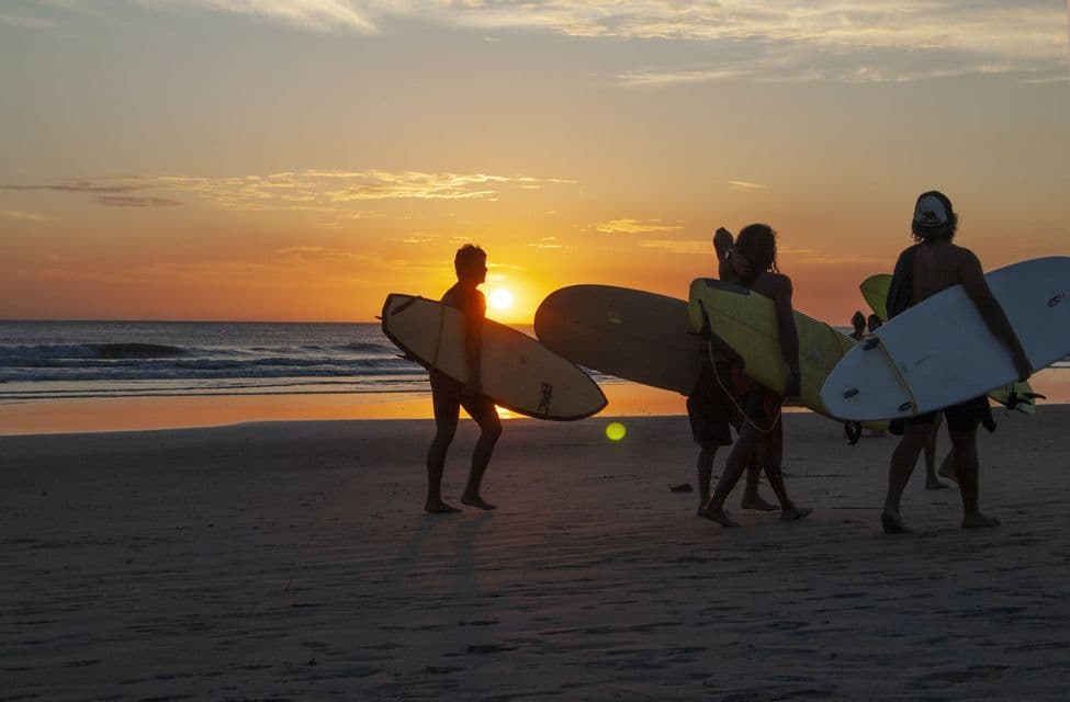 Un gruppo WeRoad di surfisti cammina su una spiaggia sabbiosa con le loro tavole da surf al tramonto.