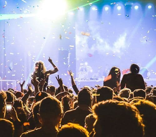 Una folla di persone con le mani alzate a un concerto, con coriandoli che cadono davanti a un palco illuminato.