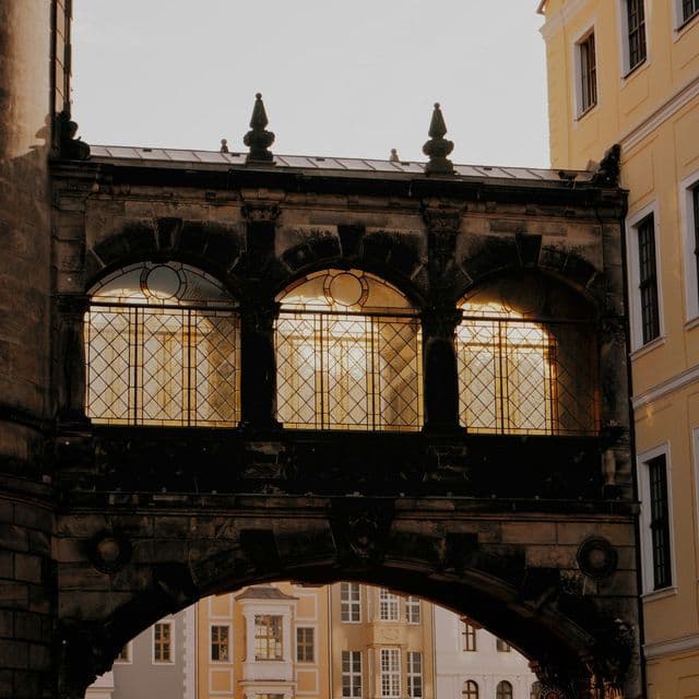 Un ponte di pietra coperto tra due edifici, con la luce del sole che illumina le sue tre grandi finestre ad arco.