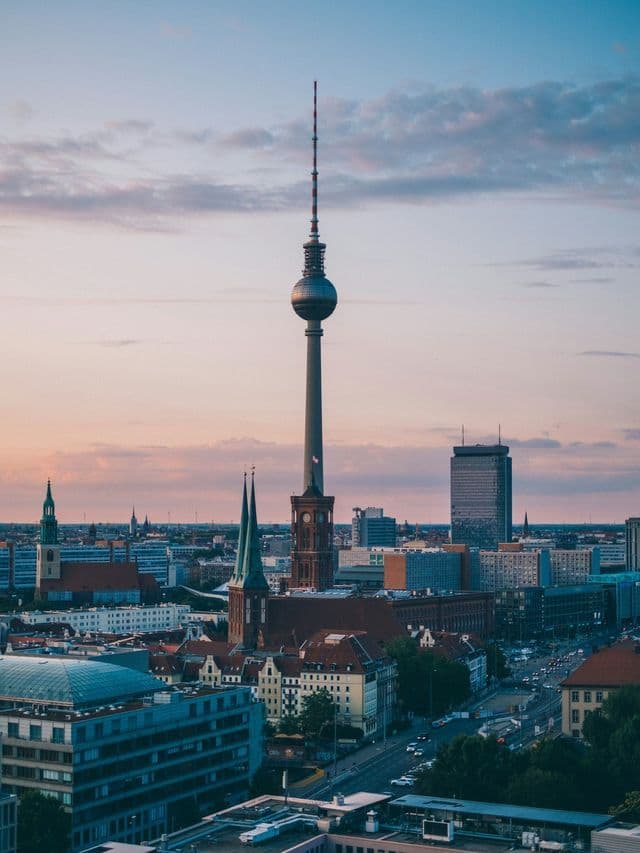 Veduta aerea di una città con una prominente torre televisiva a sfera, circondata da edifici al tramonto.