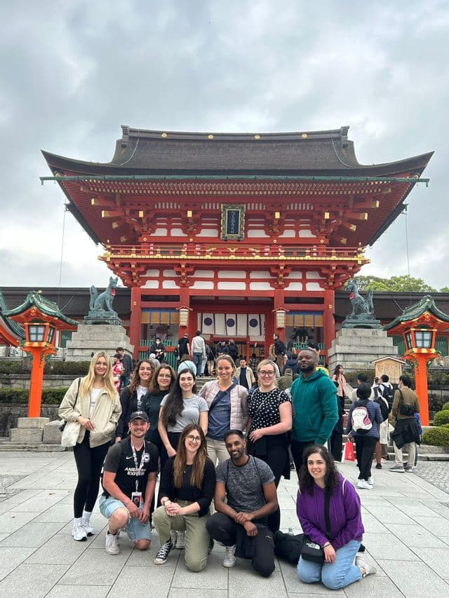 Eine WeRoad-Gruppe posiert lächelnd für ein Foto vor einem großen, traditionellen roten Tempel unter bewölktem Himmel.