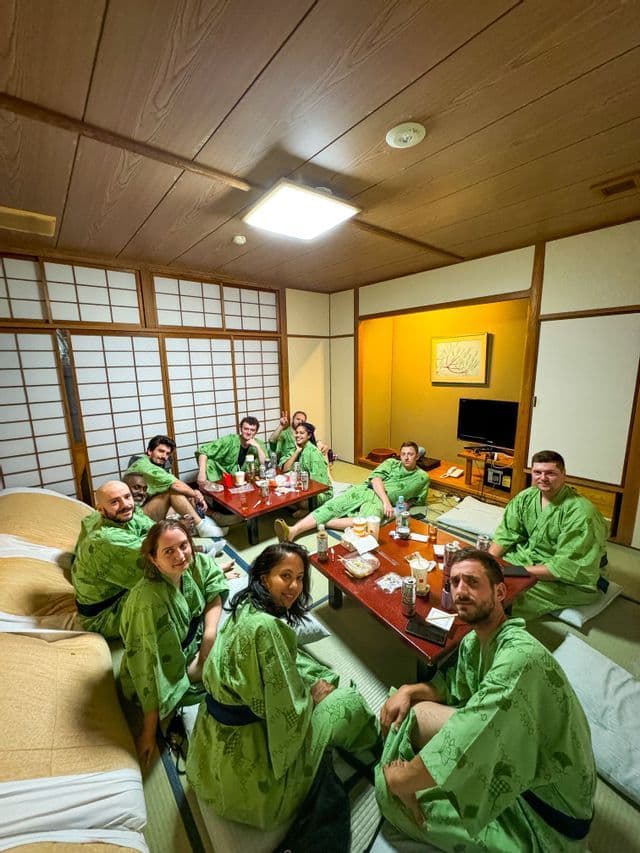 Eine WeRoad-Gruppe sitzt lächelnd in passenden grünen Yukatas in einem traditionellen japanischen Zimmer mit Tatami-Matten.