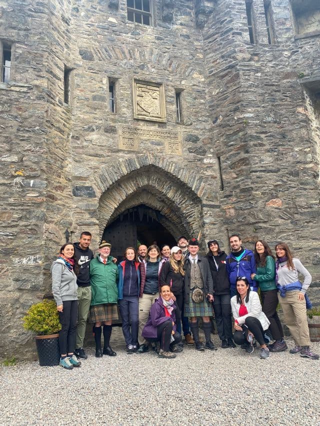 Eine WeRoad-Gruppe posiert mit Männern in Kilts am gewölbten Steineingang einer Burg.