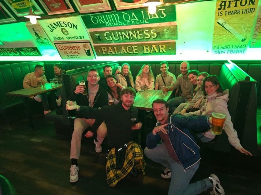 Eine WeRoad-Gruppe posiert lächelnd für ein Foto, Bierkrüge in der Hand, in einem grün beleuchteten Irish Pub.