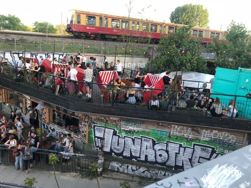 Un viaggio di gruppo WeRoad socializza in una location urbana all'aperto su più livelli con graffiti, mentre un treno passa su un binario sopraelevato.